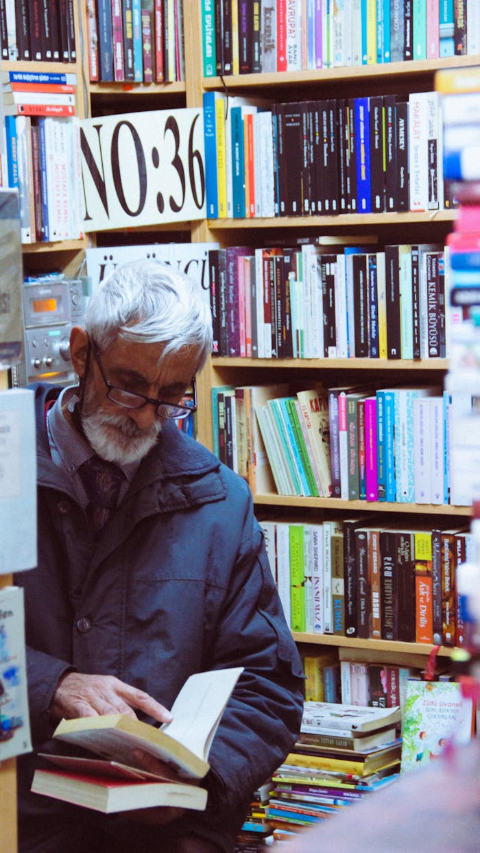 Senior man in bookstore immersed in reading among stacks of books in İstanbul, Turkey.