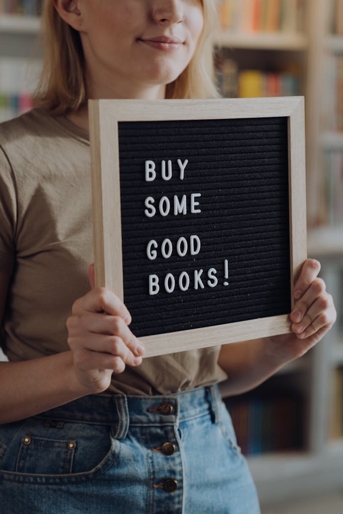 A woman holding a sign promoting book purchases, in a cozy bookstore setting.